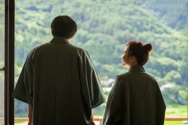 浴衣姿の二人が露台から緑豊かな山並みを眺める後ろ姿